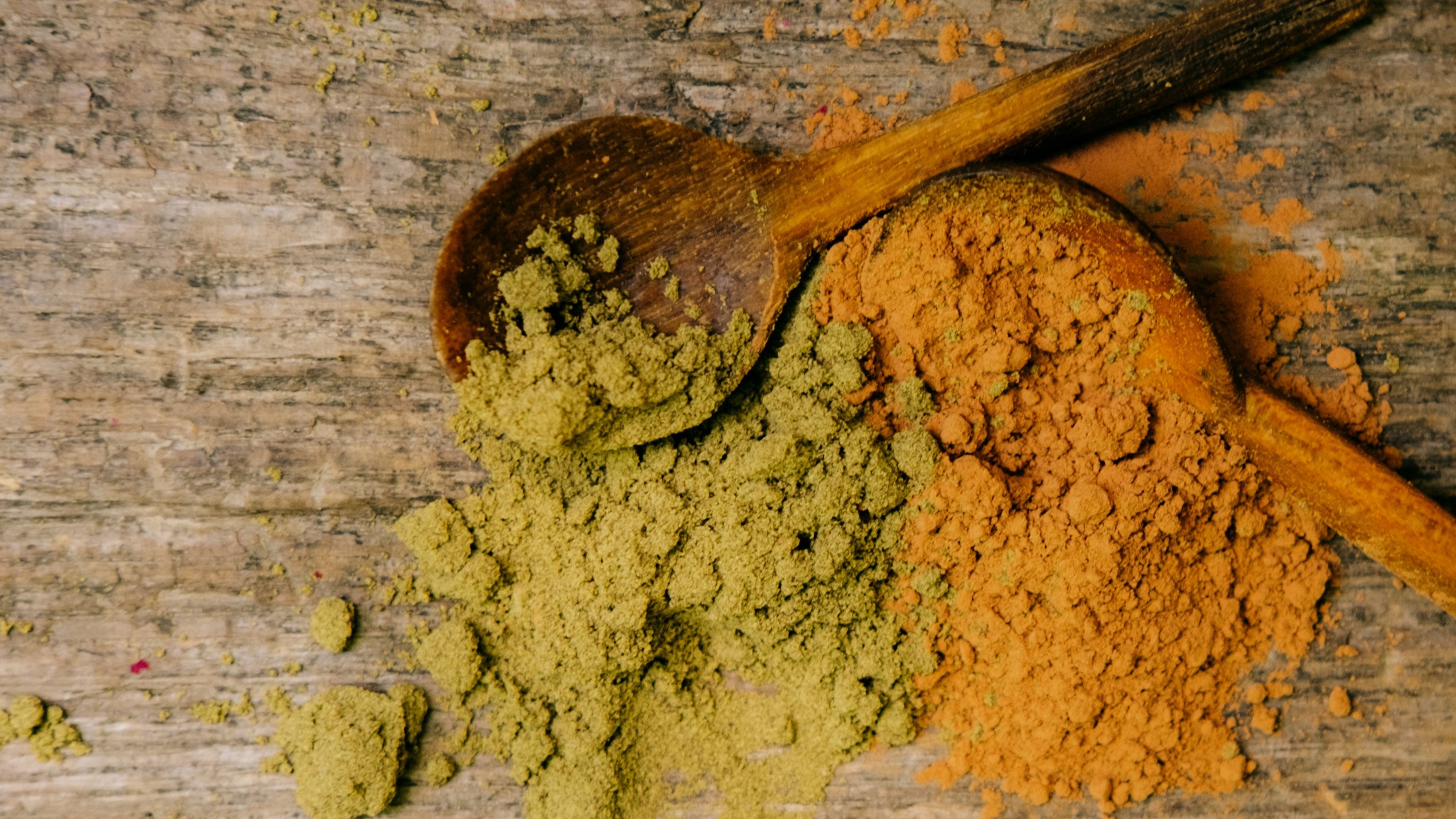 Two wooden spoons filled with green and cacao powders on a wooden surface