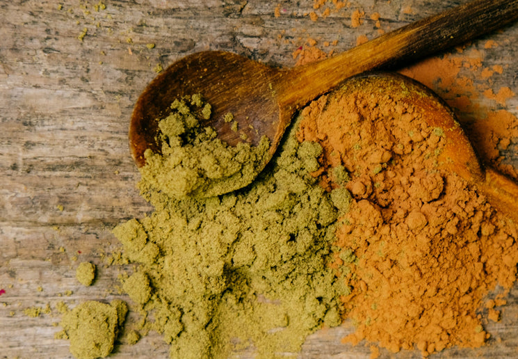 Two wooden spoons filled with green and cacao powders on a wooden surface
